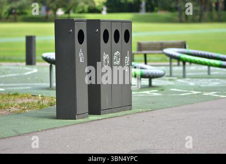 Lo smistamento dei contenitori dei rifiuti in un parco pubblico con contenitori separati per plastica, carta, vetro e rifiuti generici promuove la sostenibilità e la responsabilità Foto Stock