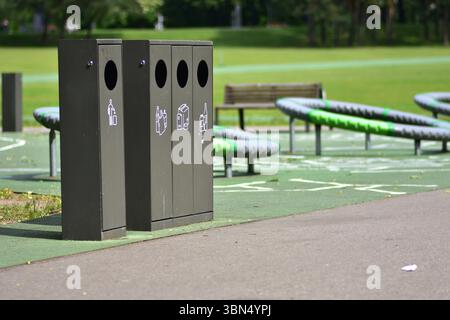 Lo smistamento dei contenitori dei rifiuti in un parco pubblico con contenitori separati per plastica, carta, vetro e rifiuti generici promuove la sostenibilità e la responsabilità Foto Stock