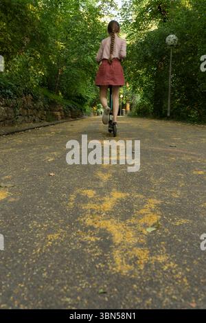 Ragazza su uno scooter. Una ragazza su uno scooter corre lungo un vicolo nel parco. Un bambino guida uno scooter nel parco Foto Stock