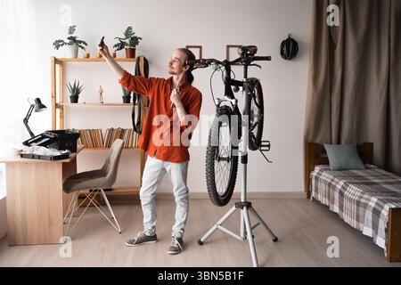 L'hipster si fa un selfie dopo aver lavorato su una bicicletta montata all'interno di casa. Copia spazio Foto Stock