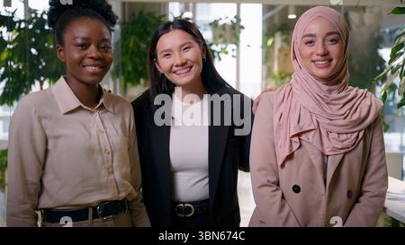 Multirazziale allegro sorridente donne d'affari tre etnie diverse amici ragazze studenti felice amichevole asiatico musulmano donne d'affari asiatiche in posa Foto Stock