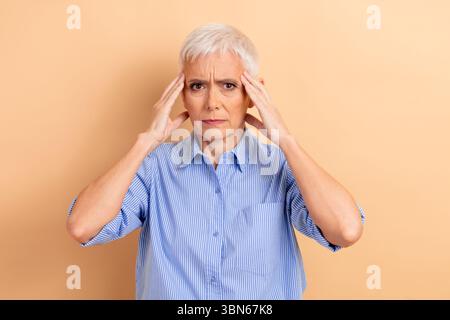 Donna d'affari matura con i capelli bianchi corti in una camicia a righe blu che mostra un'espressione premurosa su uno sfondo beige Foto Stock