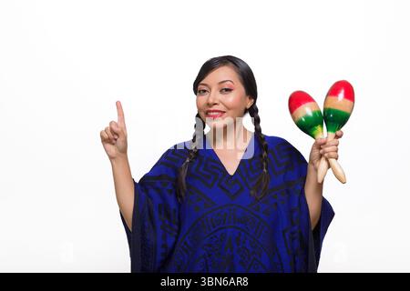 Una donna sorridente, adornata da un poncho blu a motivi geometrici, tiene le maracas mentre punta verso l'alto. Foto Stock