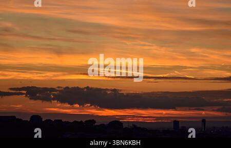 Il sole che tramonta illumina il cielo in toni arancioni, mentre le sagome di case ed edifici creano un paesaggio urbano spettacolare. Foto Stock