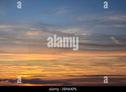 Cielo tranquillo e colorato al tramonto caratterizzato da nuvole scintillanti e una transizione graduale dal giallo dorato alle sfumature blu-grigio Foto Stock
