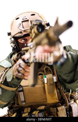 Un soldato tattico altamente equipaggiato punta un fucile durante una missione. L'individuo indossa indumenti protettivi tra cui un casco, guanti e gilet, enfatizza Foto Stock
