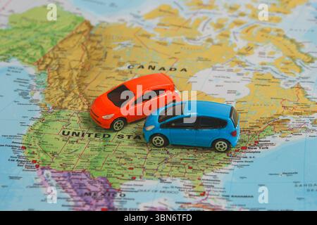 Due colorate macchinine giocattolo sulla mappa del Nord America che simboleggiano la pianificazione del viaggio, l'avventura su strada e il noleggio auto negli Stati Uniti e in Canada. Foto Stock