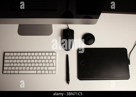 Spazio di lavoro minimalista per l'ufficio domestico con un computer desktop, una tastiera, un notebook, un tablet con penna su una scrivania bianca e pulita. Freelance a casa. Arte a casa. Foto Stock