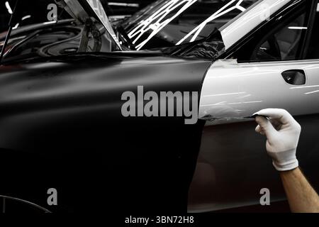 Rivestimento in vinile per auto a pannello intero. L'installazione di un involucro in vinile su larga scala trasforma l'esterno del veicolo con una pellicola nera opaca. Modifiche all'applicazione di avvolgimento per auto Foto Stock