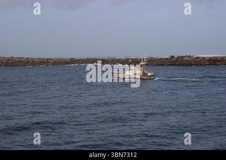 Newport, Oregon, Stati Uniti d'America - 27 febbraio 2017: Una barca della Guardia Costiera degli Stati Uniti pattuglia le acque vicino alla scogliera rocciosa, garantendo sicurezza e sicurezza nel Foto Stock