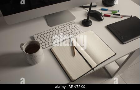 Spazio di lavoro minimalista per l'ufficio domestico con computer desktop, tastiera, notebook, tavoletta grafica, tazza con tè su una scrivania bianca pulita. Foto Stock