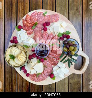 Tagliere di salumi gourmet o piatto di formaggi con vari salumi, olive, frutta e formaggio su un tagliere di legno dall'alto Foto Stock