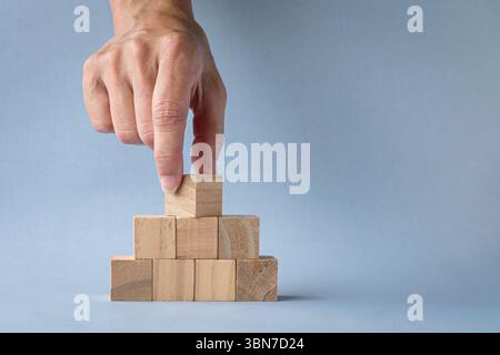 Capovolgere a mano il blocco quadrato di legno vuoto sulla parte superiore della piramide. Isolato su sfondo chiaro, spazio di copia. Foto Stock