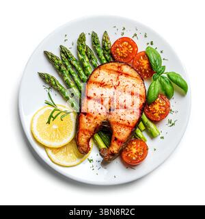 Bistecca di salmone grigliata con asparagi verdi, pomodori e fette di limone servita su piatto bianco isolato su sfondo bianco, vista dall'alto. Equilibrato sano me Foto Stock