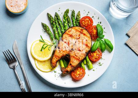 Bistecca di salmone grigliata con asparagi verdi, pomodori e fette di limone su sfondo blu, vista dall'alto. Pasto sano equilibrato, pranzo keto. Foto Stock