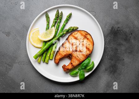 Bistecca di salmone grigliata con asparagi sul piatto su sfondo di cemento, vista dall'alto. Pranzo Keto con pesce arrosto e asparagi verdi. Foto Stock