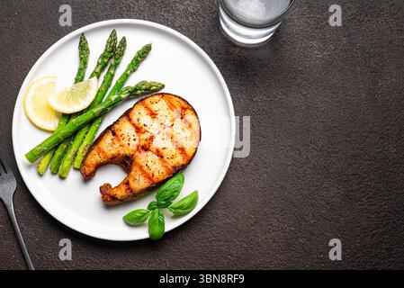 Bistecca di salmone grigliata con asparagi sul piatto, sfondo scuro, vista dall'alto, spazio per copiare. Pranzo a basso contenuto di carboidrati con pesce arrosto e verdure verdi di asparagi. Foto Stock