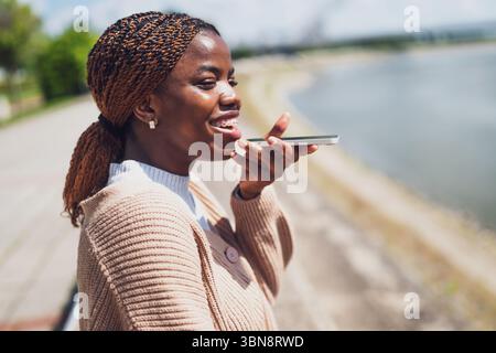 La giovane donna nera sta parlando al telefono. Lei è felice e sorridente. Foto Stock