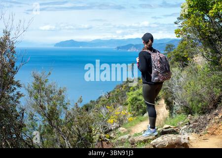 Una ragazza escursionista cammina con uno zaino lungo il sentiero da Levanto alle cinque Terre. Trekking alle cinque Terre. Foto Stock