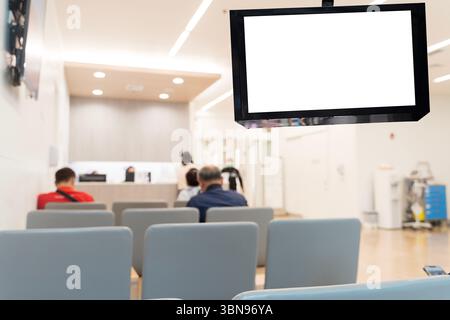 Schermo del monitor digitale vuoto nell'area di attesa dell'ospedale con persone sedute e personale infermieristico in background. Concetto per gli annunci sanitari, programma dis Foto Stock