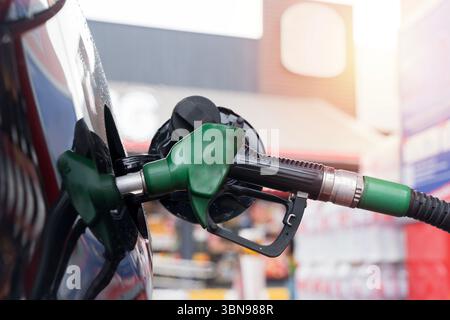 Vista ravvicinata di un ugello verde della pompa del carburante inserito nel serbatoio di un’auto presso una stazione di servizio. Rappresenta il trasporto, il rifornimento di benzina, l'energia e il carburante Foto Stock