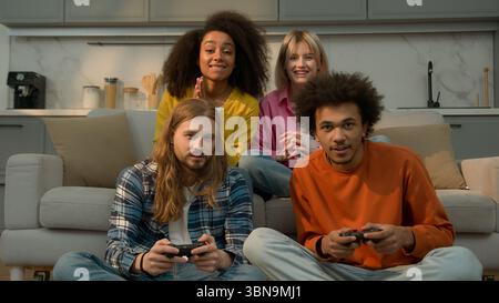 Quattro persone multirazziali amici a casa uomini caucasici maschi ragazzi video giocatori in possesso di console godendo di gioco online due afroamericani Foto Stock