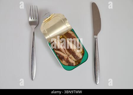 Barattolo metallico di sardine in olio su sfondo bianco con forchetta e coltello Foto Stock