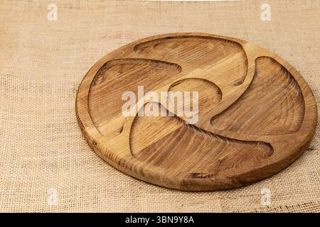 Tavola rotonda sezionata in legno con ampi scomparti intagliati per spuntini, frutta o stuzzichini, collocata su rustico tessuto burlap. Ideale per il cibo Foto Stock