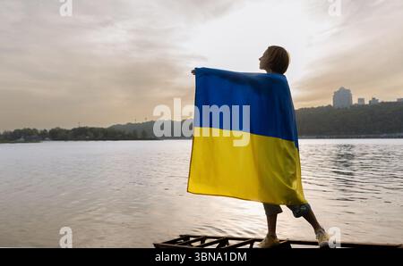 Una donna triste ha una grande bandiera Ucraina giallo-blu sulla mano tesa, pregando per l'Ucraina. Attirando l'attenzione sulle operazioni militari in Ucraina. Foto Stock
