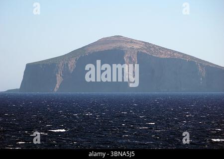 Isole greche tra Cipro e Atene, Una grande parete grigia che domina la scena. La scogliera, che sembra essere composta da roccia e possibilmente da qualche vegetazione, sorge maestosamente dall'oceano blu profondo. La superficie dell'oceano è punteggiata da piccole onde, aggiungendo un senso di movimento alla scena altrimenti ancora. Il cielo sopra è un azzurro chiaro, che fornisce uno sfondo sereno all'imponente scogliera. Il picco della scogliera è relativamente piatto, senza vegetazione visibile. L'occhio di un artista e la sua immaginazione Foto Stock
