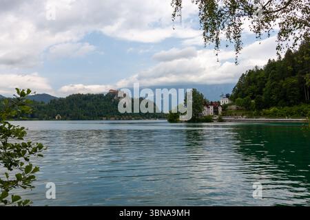 Un'ampia e pittoresca vista del lago di Bled, in Slovenia, sotto un cielo parzialmente nuvoloso. L'acqua calma e increspata riempie il primo piano Foto Stock