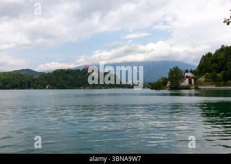 Un'ampia e pittoresca vista del lago di Bled, in Slovenia, sotto un cielo parzialmente nuvoloso. L'acqua calma e increspata riempie il primo piano Foto Stock