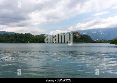 Un'ampia e pittoresca vista del lago di Bled, in Slovenia, sotto un cielo parzialmente nuvoloso. L'acqua calma e increspata riempie il primo piano Foto Stock