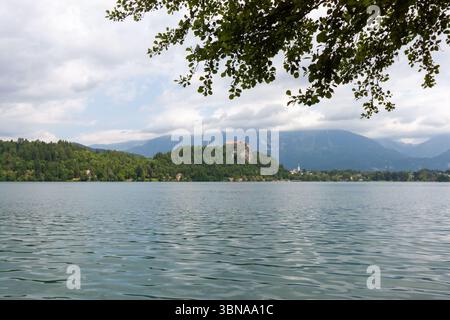 Un'ampia e pittoresca vista del lago di Bled, in Slovenia, sotto un cielo parzialmente nuvoloso. L'acqua calma e increspata riempie il primo piano Foto Stock