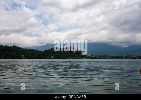 Un'ampia e pittoresca vista del lago di Bled, in Slovenia, sotto un cielo parzialmente nuvoloso. L'acqua calma e increspata riempie il primo piano Foto Stock