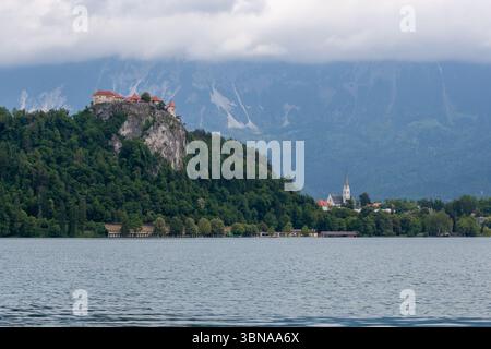 Un'ampia vista panoramica dell'iconico lago di Bled, in Slovenia, sotto un suggestivo cielo nuvoloso. Sulla sinistra, lo storico Castello di Bled si erge maestosamente in cima Foto Stock