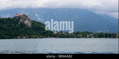 Un'ampia vista panoramica dell'iconico lago di Bled, in Slovenia, sotto un suggestivo cielo nuvoloso. Sulla sinistra, lo storico Castello di Bled si erge maestosamente in cima Foto Stock