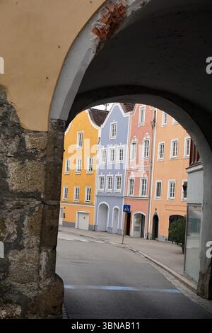 Schärding, l'affascinante gioiello barocco vicino al fiume Inn nell'alta Austria. Conosciuta per la colorata fila barocca di "Silberzeile" di case di gilde color pastello e per le mura e le porte medievali ben conservate. Una pittoresca scena di strada vista attraverso un arco costruito in pietra. L'arco incornicia la strada, che è fiancheggiata da edifici dipinti in una varietà di colori pastello, tra cui giallo, blu, rosa e pesca. Gli edifici presentano uno stile architettonico tradizionale con tetti a tetto spiovente e finestre con cornici bianche. Un piccolo edificio di colore chiaro e' visibile sul lato destro della strada. La strada stessa lo è Foto Stock