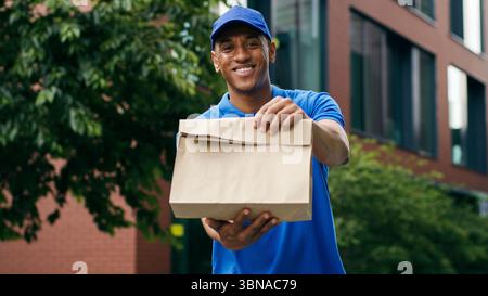 Ritratto felice sorridente guardando la macchina fotografica in piedi all'aperto il corriere afroamericano consegna di cibo maschio uomo servizio di mantenimento ordine di acquisto Foto Stock