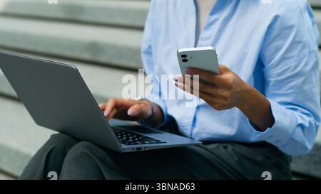Irriconoscibile studentessa afroamericana donna d'affari donna d'affari donna seduta in città all'aperto lavora online scrivendo un pc portatile Foto Stock