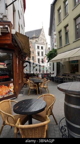 Anversa, la seconda città belga più grande, situata sul fiume Schelda in Belgio, Una strada acciottolata fiancheggiata da edifici. La strada e' adornata da aree salotto esterne, che includono tavoli e sedie, e alcune persone sono visibili, suggerendo un'atmosfera vivace. Sul lato sinistro della strada, un edificio in legno con una tenda beige mostra un cartello con la scritta "Kipaan's". Sul lato destro è visibile un edificio con una tenda verde e un cartello con la scritta "Mamma". Sul lato destro dell'immagine si trova una grande canna di legno. Gli edifici sono principalmente in tonalità di bianco, beige e marrone, Foto Stock