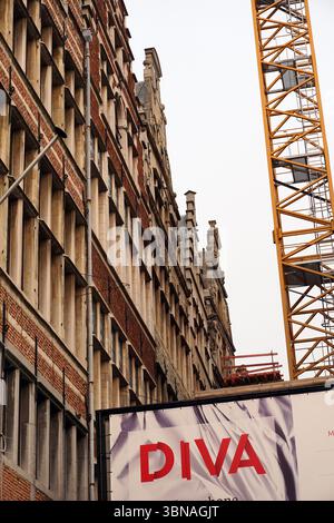 Un paesaggio urbano con un alto e ornato edificio in mattoni caratterizzato da intricati dettagli architettonici, tra cui elementi decorativi sulla linea del tetto. Una gru da cantiere, dipinta di giallo brillante, è posizionata sul lato destro dell'immagine, suggerendo uno sviluppo in corso. Un grande banner con la parola "DIVA" in grassetto rosso viene visualizzato in primo piano, probabilmente pubblicizzando un prodotto o un servizio. Il cielo è coperto, proiettando una luce soffusa sulla scena. La prospettiva dell'immagine è da un'angolazione bassa, guardando verso l'alto l'edificio e la gru, enfatizzando la loro altezza e grandezza., Antwe Foto Stock