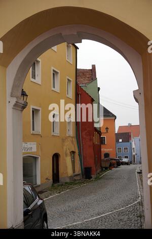 Schärding, l'affascinante gioiello barocco vicino al fiume Inn nell'alta Austria. Conosciuta per la colorata fila barocca "Silberzeile" di case delle corporazioni color pastello e per le mura e le porte medievali ben conservate, Una pittoresca strada acciottolata, vista attraverso un arco. La strada è fiancheggiata da edifici di vari colori, tra cui giallo, arancione, rosso e blu, con alcuni segni di età e di resistenza agli agenti atmosferici. Gli edifici sono principalmente alti due piani, con alcuni che hanno finestre multiple. Una macchina nera è parcheggiata sul lato sinistro della strada, e alcune auto sono parcheggiate sul lato destro. Il cielo e' coperto, getta un Foto Stock
