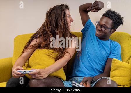 Un uomo prende in giro la sua ragazza dopo aver vinto un videogioco, entrambi ridendo sul divano a casa. Foto Stock