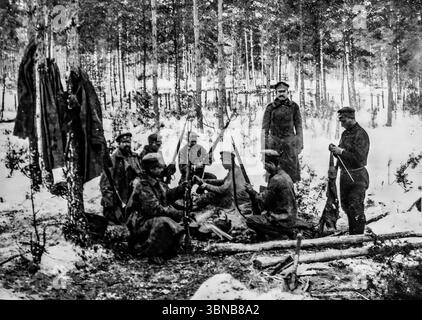 I soldati russi puliscono i loro fucili all'aperto in una foresta innevata durante la prima guerra mondiale, nonostante il freddo, sembrano a loro agio, seduti sui tronchi e rilassati come in una caserma. Fotografata da Pierre Choumoff, questa immagine cattura la vita militare quotidiana sul fronte orientale durante l'inverno. Pubblicato su l’Illustration, rivela la resistenza e la routine delle truppe russe in condizioni difficili Foto Stock