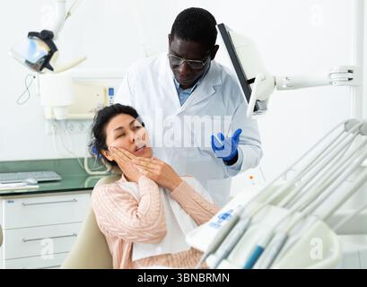 Paziente donna che è venuto ad un appuntamento con un dentista maschio è seduto in una sedia dentale in clinica ufficio, mostrando quale lato del suo dente dolori Foto Stock