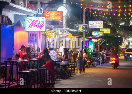 Scena di strada di notte con bar, posti a sedere all'aperto, donne, sotto vari cartelli al neon, Hua Hin, Thailandia Foto Stock