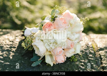 Un bouquet di rose rosa e bianche poggia su di una pietra, circondata da verde tenue in una calda luce serale. Foto Stock