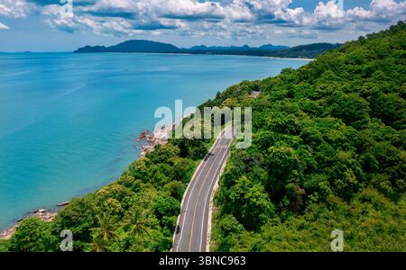 Vista aerea della strada tra palme da cocco e il grande oceano di giorno a Nakhon si Thammarat, Thailandia Foto Stock