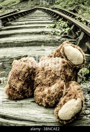 Un orsacchiotto marrone giace su vecchi binari ferroviari in legno. Foto Stock